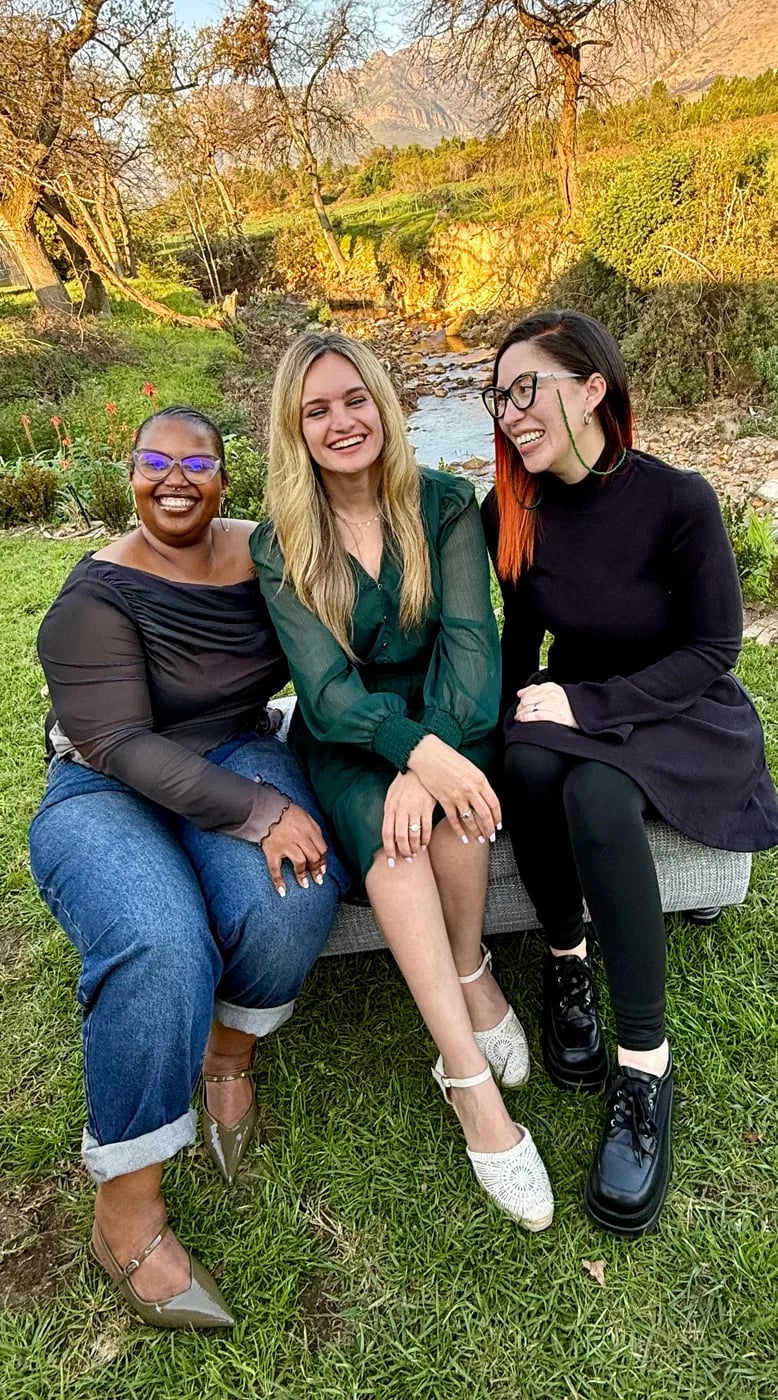 The three practitioners on a bench beside the stream, mountains behind them.